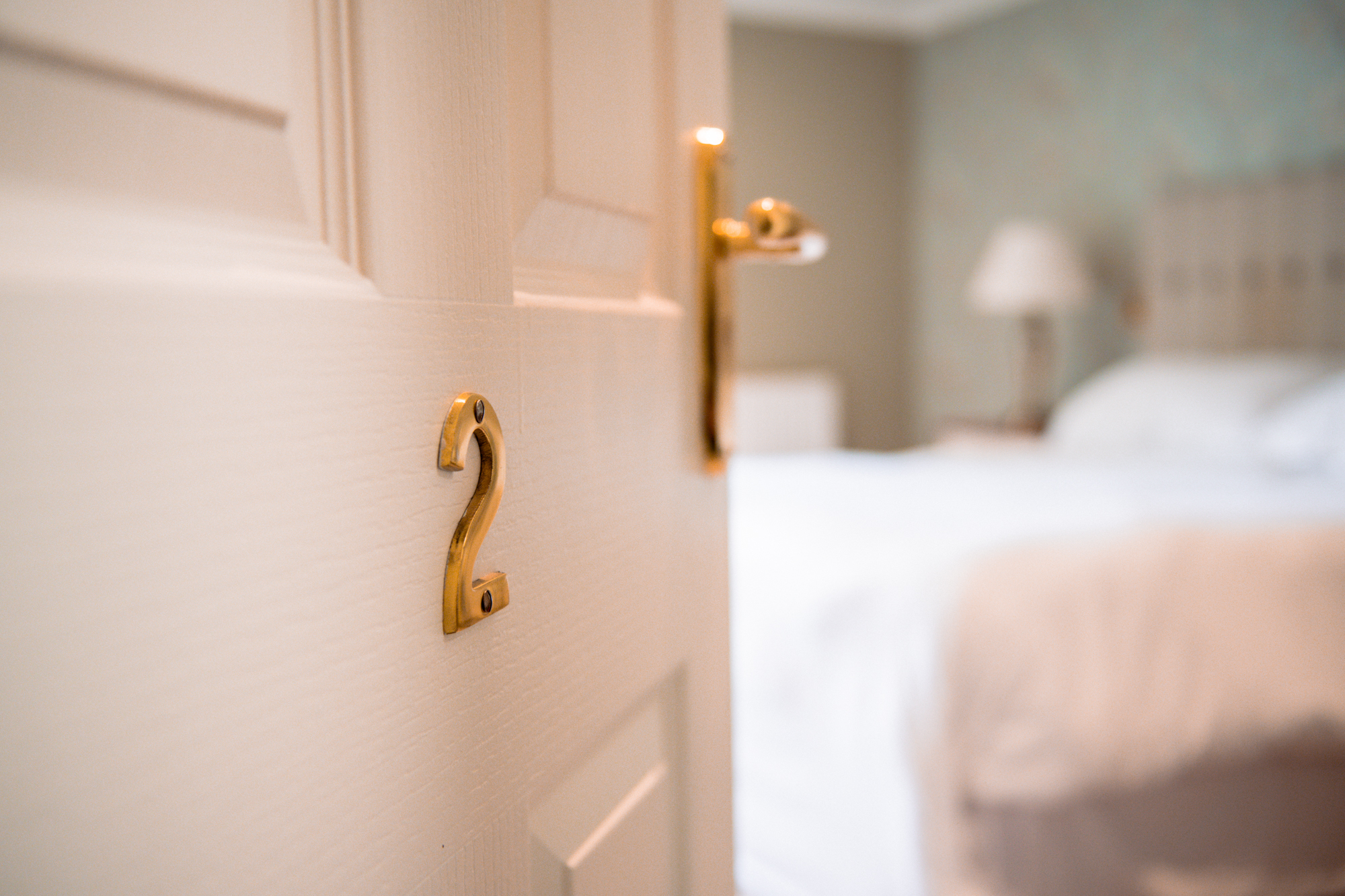 Image of a white door with the number two one it, open to a bedroom with a blurred view of the bed.