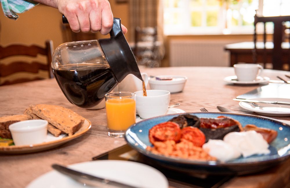 a selection of breakfast foods on a table with a hand pouring a coffee pot